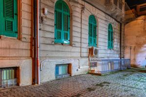 a building with green shuttered windows and a stone courtyard at Tribunale Basement Apartment in Messina