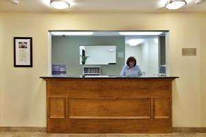 Candlewood Suites Lake Charles-Sulphur, an IHG Hotel في سولفور: امرأة تقف في مكتب الاستقبال في غرفة مستشفى