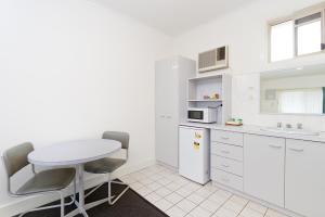 eine kleine weiße Küche mit einem Tisch und Stühlen in der Unterkunft Carrum Downs Motel in Carrum Downs