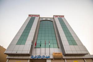 een hoog gebouw met vlaggen ervoor bij Waha AL Mudaif Serviced Apartments in Tabuk