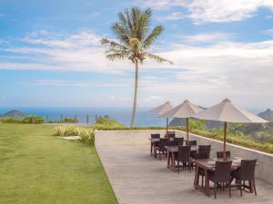 a patio with tables and umbrellas and the ocean at Selong Selo Resort and Residences in Selong Belanak
