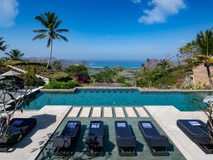 a swimming pool with lounge chairs and the ocean at Selong Selo Resort and Residences in Selong Belanak