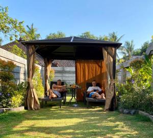 3 Männer sitzen unter einem Pavillon im Garten in der Unterkunft Vila Troja Kubu in Tulamben