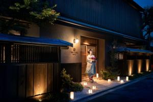 THE JUNEI HOTEL Kyoto Imperial Palace West في كيوتو: امرأة تقف خارج مبنى مع أضواء