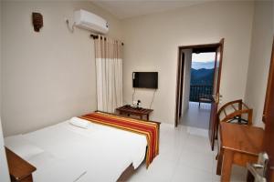 1 dormitorio con cama, TV y balcón en Jack Tree Lodge, en Kandy