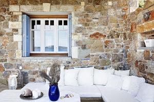 Lithea Villas and Studios by the Sea في أغيوس بطرس ألونيسوس: أريكة بيضاء أمام جدار حجري مع نافذة