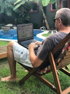 a man sitting in a chair with a laptop on his lap at Pousada Tatuapara in Praia do Forte