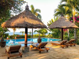 una piscina del resort con sedie, ombrelloni e tavolo di Villa Bidadari - Bali Sea Villas Beachfront and private pool a Pengastulan