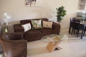 ein Wohnzimmer mit einem braunen Sofa und einem Glastisch in der Unterkunft OR Tambo Self Catering Apartments, The Willows in Boksburg