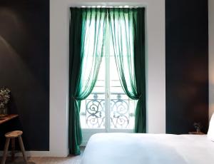 a bedroom with a bed and a window with green curtains at Hotel des Grands Boulevards in Paris