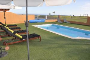 a swimming pool with lounge chairs and an umbrella at Villa Surprise only Solar Energy in Caleta De Fuste