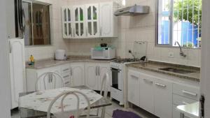 uma cozinha com armários brancos, uma mesa e um micro-ondas em Casa temporada na praia em Ubatuba