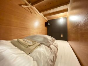 a bed with white sheets and a wooden wall at HOTEL&HOSTEL HARU in Kanoya