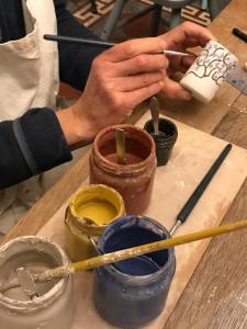 una persona pintando una olla en una mesa de madera con pinceles de pintura en Villa Toscane - Atelier d'Artistes et B&B à 20 mn de Toulouse en Azas