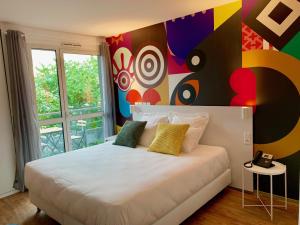 a bedroom with a large bed with a colorful wall at Brit Hotel Bordeaux Arena in Latresne