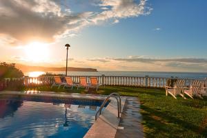 a pool with chairs next to the ocean at sunset at Apartamentos El Caserio in Suances