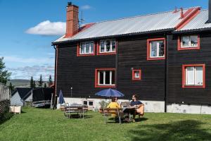 two people sitting under an umbrella in front of a house at North Mountain Lodge in Funäsdalen