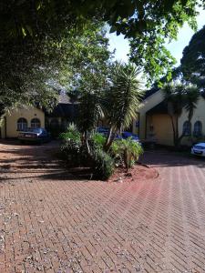 a brick driveway with palm trees in front of a building at Rocky Ridge Guest House 2 SELF CATERING - No Alcohol allowed in Roodepoort