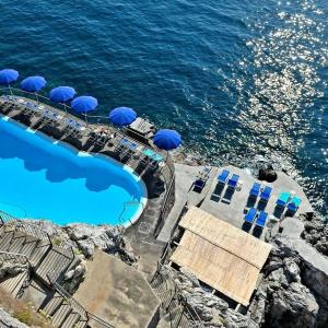 a swimming pool with blue umbrellas and the ocean at Hotel Luna Convento in Amalfi