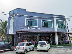 dos autos estacionados frente a un edificio azul en Hotel Ikhwan, en Kota Bharu