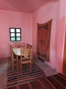 una mesa y sillas en una habitación con paredes rosas en Auberge Restaurant Les Coquelicots, en Aït Tamellil