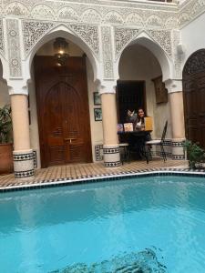 una mujer sentada en una mesa junto a una piscina en Riad Abaka hotel & boutique, en Marrakech