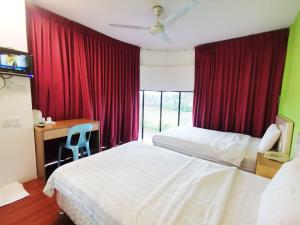 a bedroom with two beds and a desk and red curtains at Homestay Kuching Hotel in Kuching