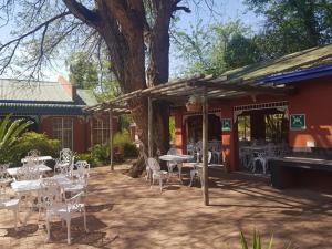 un patio con mesas y sillas blancas y un árbol en Garden View Lodge en Mafikeng
