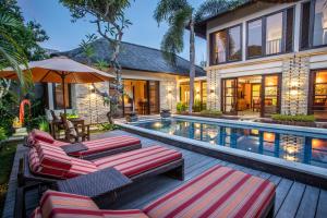 an outdoor pool with lounge chairs and an umbrella at Villa Saffron Seminyak Bali in Seminyak