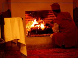 Un uomo seduto accanto al fuoco in un camino di Riad Shama Suites & Spa a Marrakech