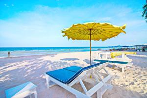 einen Strand mit einem gelben Sonnenschirm, Stühlen und einem Tisch in der Unterkunft Baan Bayan - Hua Hin - SHA Extra Plus in Hua Hin