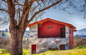 ein rotes Gebäude mit einem Baum davor in der Unterkunft Apartamentos Vega Rodiles el campu in Villaviciosa