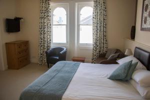 a bedroom with a bed and a chair and two windows at The Sheldon B&B - FREE private parking in Eastbourne
