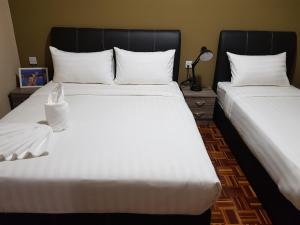 two beds in a room with white sheets and pillows at Sandra Homestay in Tawau