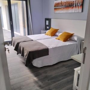 1 dormitorio con 2 camas con sábanas blancas y almohadas amarillas en Carballos Altos-Apartamentos Turísticos, en Arzúa
