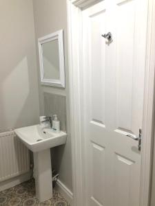 Baño blanco con lavabo y puerta en Beechwood Garden Suite, en Newtownabbey
