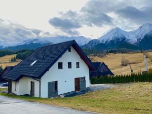 a white house with a black roof with mountains in the background at Villa Jarka Rent in Ždiar