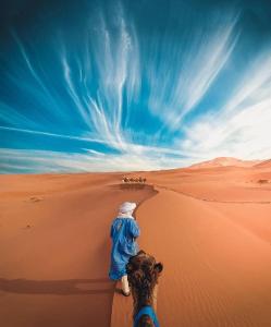 a man walking in the desert with a camel at Désert Man luxury Camp in Merzouga
