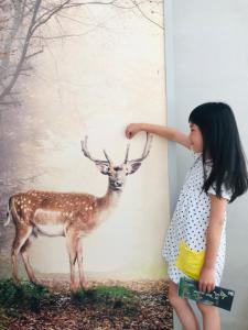Una bambina che guarda un cervo dipinto su un muro di Yishan Village a Jincheng