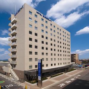 a large white building with a blue sign in front of it at Hotel Mark-1 Tsukuba in Tsukuba