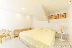 a white bedroom with a bed and a chair at Pipa Atlântico Bungalow 41 in Pipa