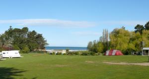 a field with a tent and a trailer and the ocean at Motels by the Moeraki Boulders Holiday Park in Hampden