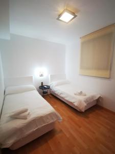 Habitación con 2 camas, paredes blancas y suelo de madera. en Hostal Quinta Santillan en San Fernando de Henares