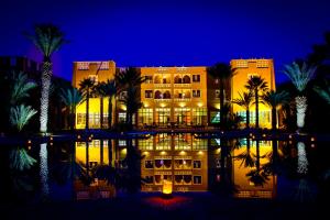 a hotel with palm trees and a pool at night at Erfoud Palace in Erfoud