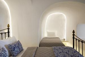 a bedroom with two beds and a white wall at La Perla Villas and Suites - Adults Only in Oia