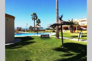 une piscine avec un banc et des parasols dans une cour dans l'établissement APARTAMENTO VISTA MAR LA TORTUGA, à Tarifa