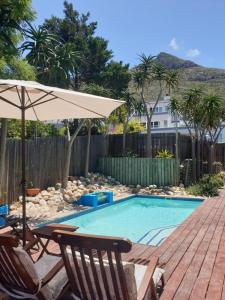 a swimming pool with two chairs and an umbrella at Hout Bay Breeze Guest House in Hout Bay
