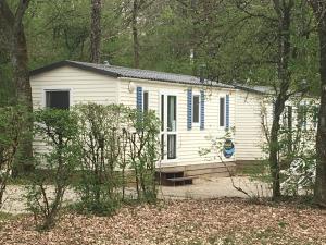ein weißes Cottage mit blauen Rollläden in einem Wald in der Unterkunft Camping de la Croix d'Arles in Bourg