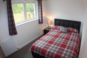 a bedroom with a bed with a plaid blanket and a window at 2 Dellmhor Cottages in Aviemore