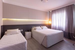 two beds in a hotel room with white sheets at Hotel Melo in Balneário Camboriú